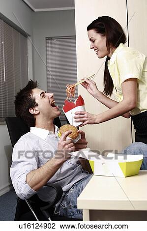 Office worker feeding her colleague at desk View Large Photo Image Stock Image - Office worker feeding her colleague at desk. Fotosearch