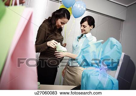 Stock Image - Pregnant office worker with colleague at party. Fotosearch