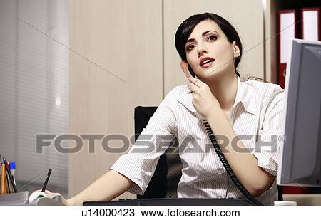 Stock Image - Businesswoman at desk on phone. Fotosearch