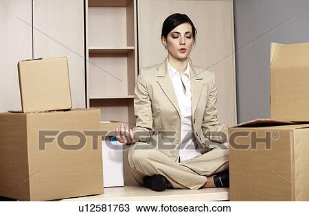 Stock Image - Businesswoman on desk among boxes meditating. Fotosearch