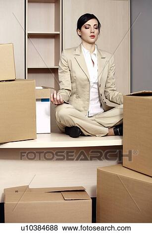 Stock Photo - Businesswoman on desk among boxes meditating. Fotosearch