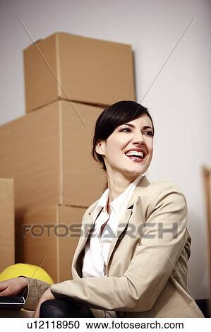Stock Image - Businesswoman with laptop among boxes. Fotosearch