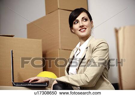 Stock Image - Businesswoman with laptop among boxes. Fotosearch