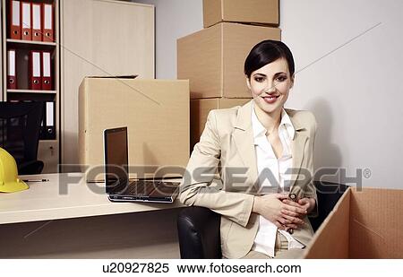 Stock Photography - Businesswoman with laptop among boxes. Fotosearch