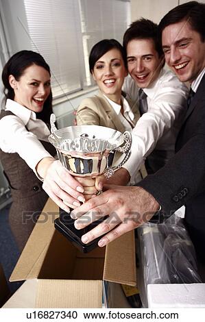 Stock Image - Four business people holding trophy in office. Fotosearch