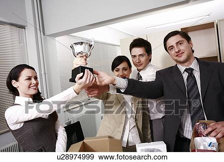 Four business people holding trophy in office View Large Photo Image Stock Photo - Four business people holding trophy in office. Fotosearch