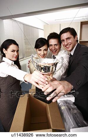 Four business people holding trophy in office View Large Photo Image Stock Photograph - Four business people holding trophy in office. Fotosearch