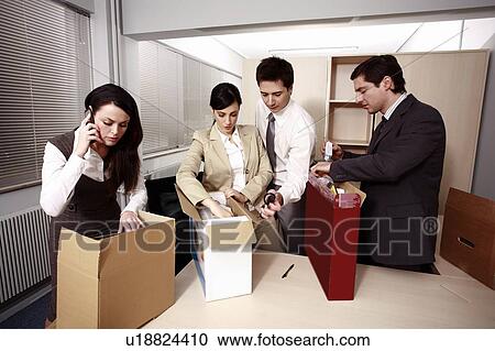 Stock Image - Four business people unpacking boxes in office. Fotosearch