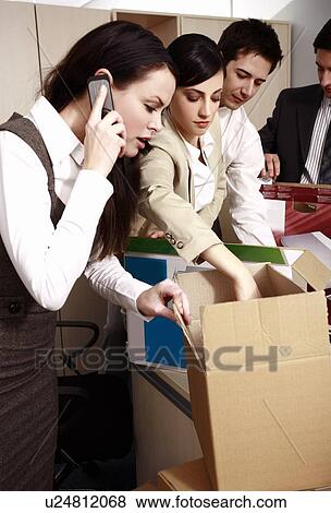 Stock Photo - Four business people unpacking boxes in office. Fotosearch