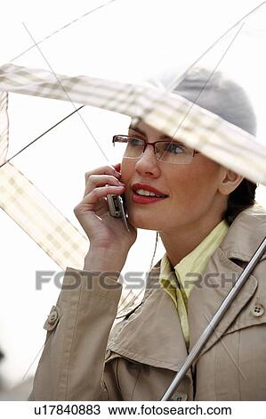 Stock Image - Businesswoman on cell phone with umbrella. Fotosearch