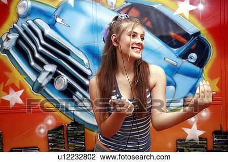Stock Image - Female teenager with mp3 player in front of graffiti. Fotosearch