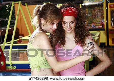 Stock Photo - Female teenagers taking picture of themselves with cell phone camera. Fotosearch