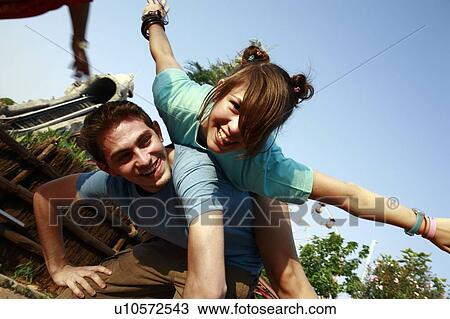 Stock Image - Teenage couple playing on piggy back in amusement park. Fotosearch