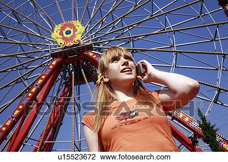 Stock Image - Female teenager on cell phone at Ferris wheel in amusement park. Fotosearch