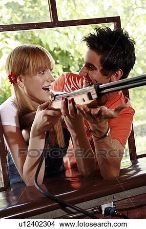 Picture - Teenage couple at shooting game in amusement park. Fotosearch