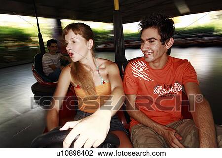 Stock Image - Teenage couple in bumper car in amusement park. Fotosearch