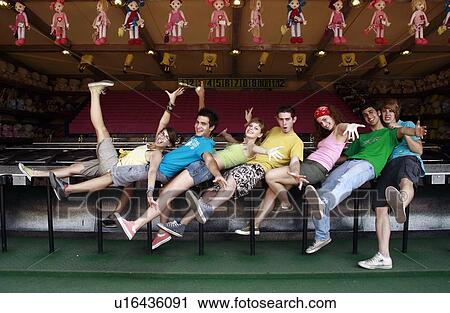 Stock Image - Teenagers posing in front of game in amusement park. Fotosearch