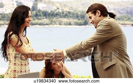 Stock Image - Man and woman shaking hands at seaside meeting. Fotosearch
