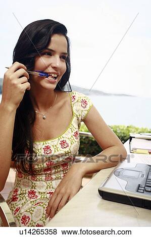 Stock Photo - Woman at seaside table with pen in her mouth. Fotosearch
