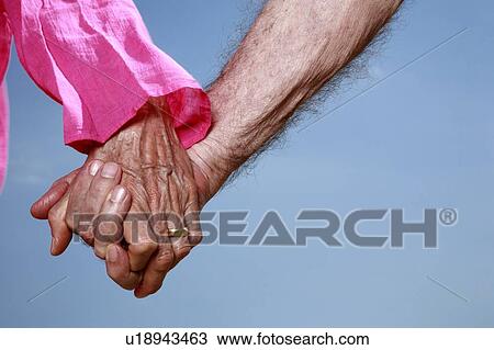 Stock Image - Closeup of senior couple holding hands. Fotosearch