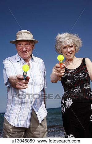 Stock Photo - Senior couple on beach with water guns. Fotosearch