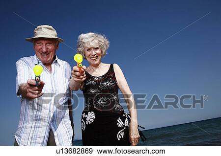Stock Photo - Senior couple on beach with water guns. Fotosearch