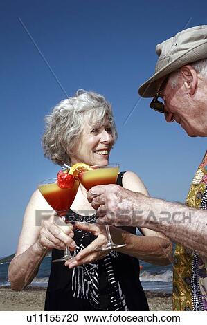 Stock Image - Senior couple with cocktails on beach. Fotosearch