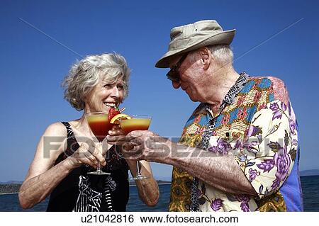 Stock Photograph - Senior couple with cocktails on beach. Fotosearch
