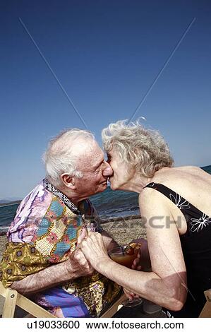 Stock Image - Senior couple with on beach kissing. Fotosearch