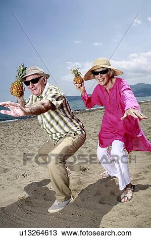 Stock Image - Senior couple with pineapples on the beach. Fotosearch