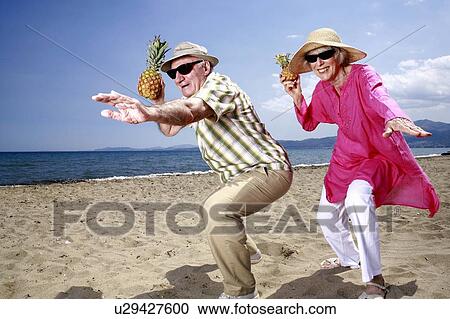 Stock Image - Senior couple with pineapples on the beach. Fotosearch