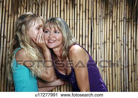 Stock Image - Daughter whispering in mother's ear. Fotosearch