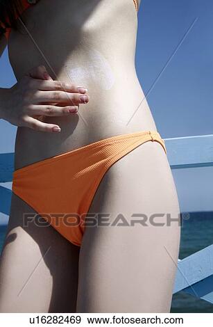 Stock Photo - Female young adult applying suntan lotion. Fotosearch