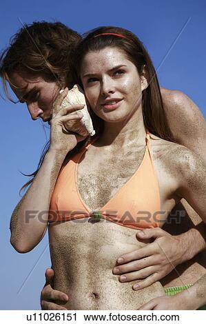 Stock Image - Female young adult with seashell and male young adult. Fotosearch