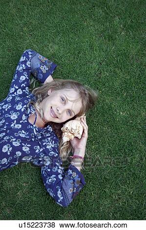 Stock Photo - Girl on grass listening to seashell. Fotosearch