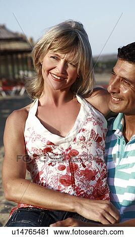 Stock Image - Mature adult couple sitting on beach. Fotosearch