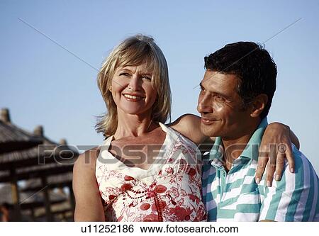 Stock Photograph - Mature adult couple sitting on beach. Fotosearch