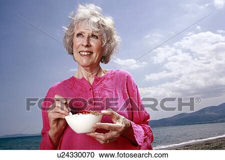 Female senior eating yogurt and fruit on the beach View Large Photo Image Stock Image - Female senior eating yogurt and fruit on the beach. Fotosearch