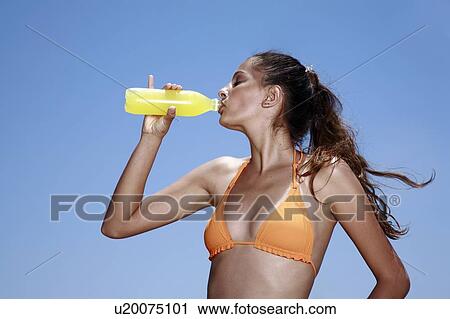 Stock Image - Female young adult drinking juice in bikini. Fotosearch
