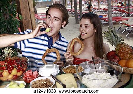 Stock Image - Young adult couple at breakfast holding sesame bread rings. Fotosearch