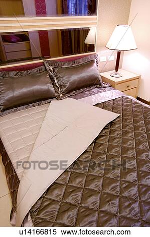 Stock Photography - Close-up of bed with pillows and quilt by side table with lamp. Fotosearch