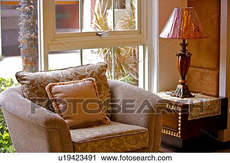 Stock Image - Single sofa with lamp on side table by window. Fotosearch