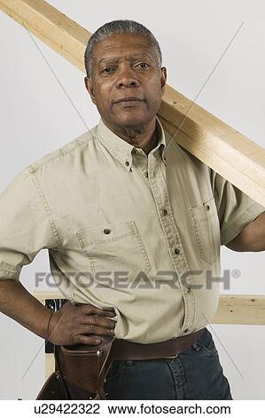Stock Image - African American Man Doing Home Improvement, Carrying 2x4 Lumber Over Shoulder, Vancouver, BC. Fotosearch