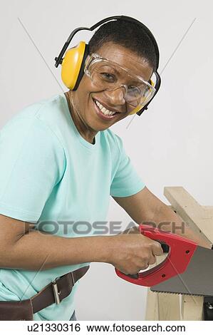 Stock Photograph - African American Woman Doing Home Improvement, Cutting Lumber With a Hand Saw, B. C.. Fotosearch