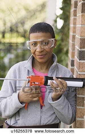 Stock Photo - African American woman using a caulking gun, Vancouver, BC. Fotosearch