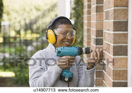 Stock Image - African American woman using a hand drill, Vancouver, BC. Fotosearch