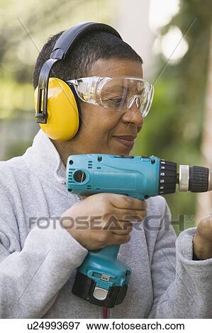 Stock Photo - African American woman using a hand drill, B. C.. Fotosearch