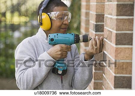 Stock Photograph - African American woman using a hand drill, Vancouver, BC. Fotosearch