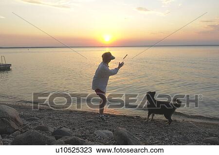 Stock Image - Woman with dog at beach Clear Lake; Canada, Manitoba, Riding Mountain National Park. Fotosearch