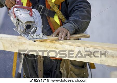 Construction worker cutting a piece of wood with a skill saw.; Canada, Ontario, Hamilton (Composting Facility) View Large Photo Image Stock Photo - Construction worker cutting a piece of wood with a skill saw.; Canada, Ontario, Hamilton (Composting Facility). Fotosearch